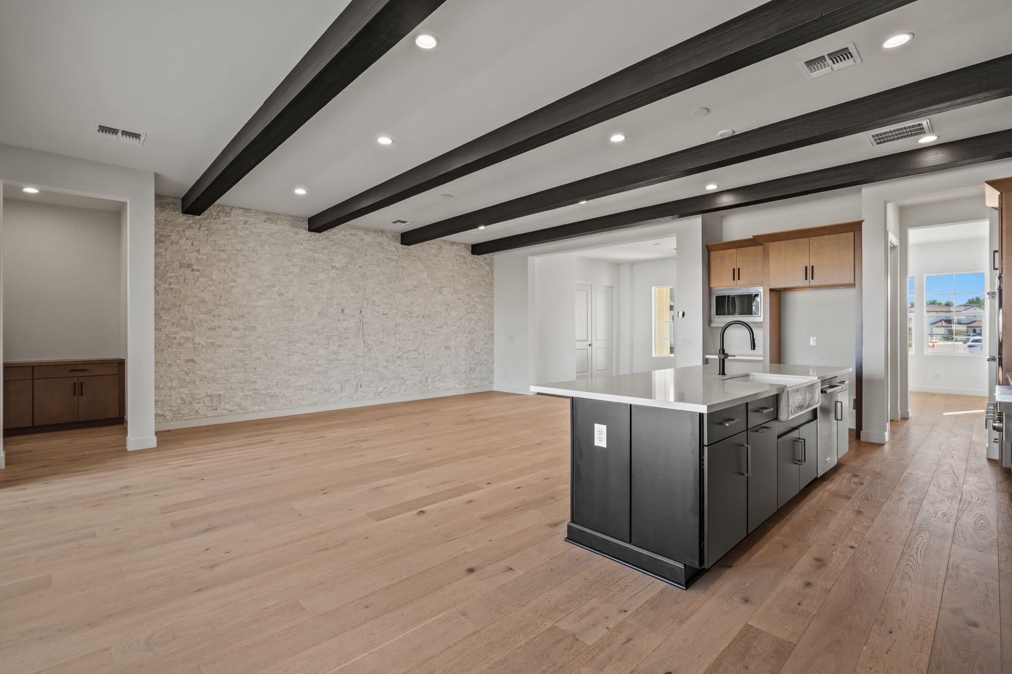 Great room with stack-stone wall, beamed ceiling, white oak floors and kitchen island